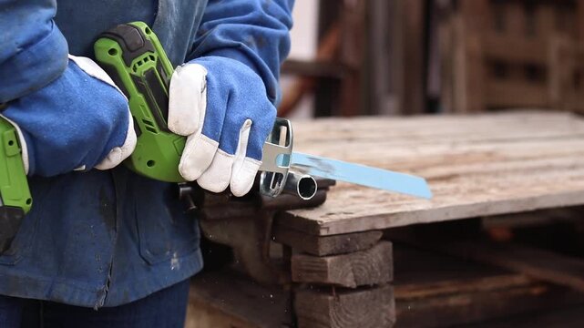 Cordless reciprocating saw cuts metal pipe. A craftsman in protective gloves uses a cordless reciprocating saw (electric knife) to saw a thin pipe. Working with a power tool. Close-up of work