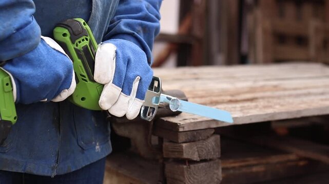 Cordless reciprocating saw cuts metal pipe. A craftsman in protective gloves uses a cordless reciprocating saw (electric knife) to saw a thin pipe. Working with a power tool. Close-up of work
