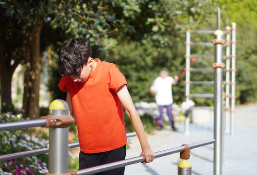 LTeenage boy exercising on parallel bars and grandfather in the background using resistance bands