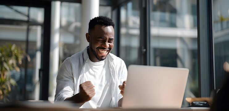 Excited Young Man Celebrating Success While Working on Laptop in Modern Office.