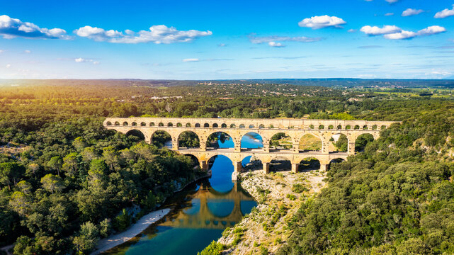 Aqueduct of Pont du Gard arches over the river, showcasing the rich history of Vers-Pont-du-Gard, France. Ancient aqueduct of Pont du Gard spans the peaceful river in Vers-Pont-du-Gard, France.