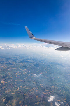View of the wing of an airplane flying above the clouds at high altitude under a blue sky from the passenger window. In flight over Europe. View of jet airplane wing flying in blue sky over clouds.