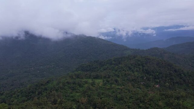 Aerial drone view of low clouds and mist drifting over green mountain slopes and layered hills of Kerala