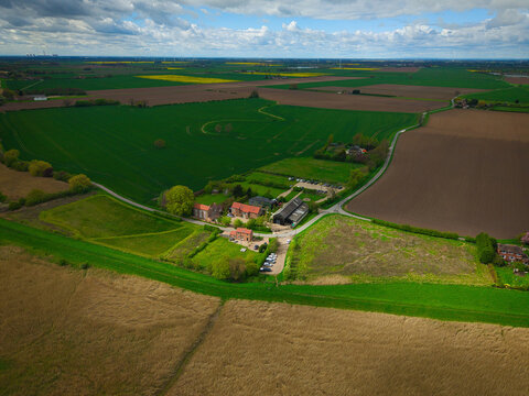 Aerial view of Trent Falls area featuring lush green agricultural fields, rural farm buildings, and a winding road under a cloudy sky Goole, United Kingdom.