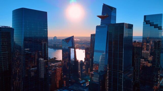 Modern glass skyscrapers in Manhattan at sunset with sun flare. Aerial view of tall glass office buildings and triangular observation deck during golden hour in New York City.