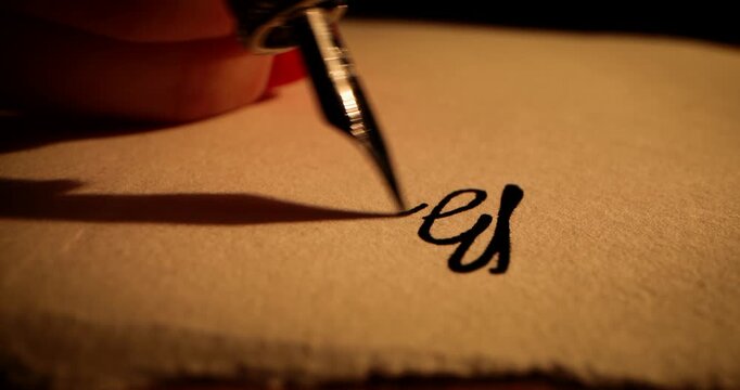 closeup of hand writing letter with vintage quill pen and ink on old parchment paper by candlelight
