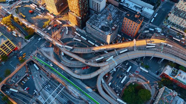 Aerial view of complex bus terminal ramps in urban city. Top down shot of multi-level concrete ramps with white buses during golden hour sunlight in a dense urban area.