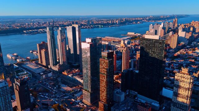 Modern towers and riverfront development in New York City. New architectural developments and glass skyscrapers near the water during a vibrant sunset over the city.