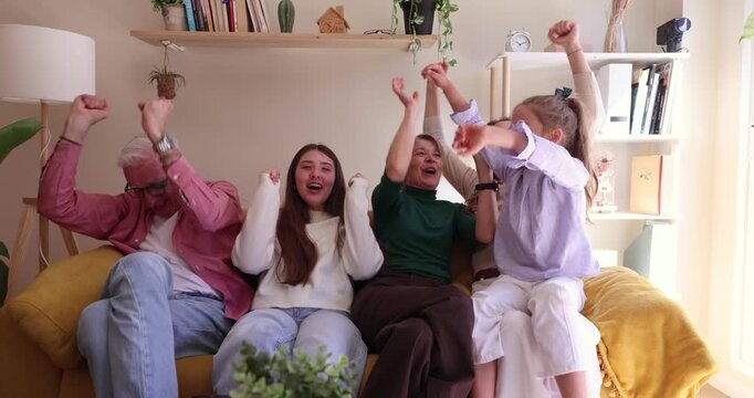 Excited three generation family sitting together on a yellow sofa, watching a sports match on television, cheering, and celebrating their favorite team scoring a winning goal at home