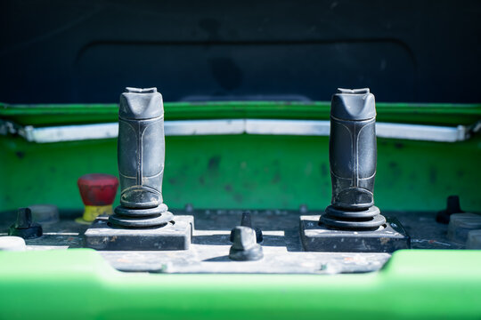 Dual joystick controls on green construction machine operator panel, industrial equipment cockpit detail for machinery handling, fleet maintenance and training