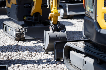 Multiple compact excavators on gravel with trench buckets, blades and rubber tracks, industrial machine detail for earthmoving and site operations © K