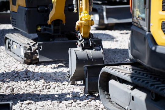 Multiple compact excavators on gravel with trench buckets, blades and rubber tracks, industrial machine detail for earthmoving and site operations