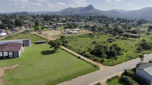 Drone flies west over two different fairgrounds with view of Execution Rock on sunny morning in Lobamba, Eswatini
