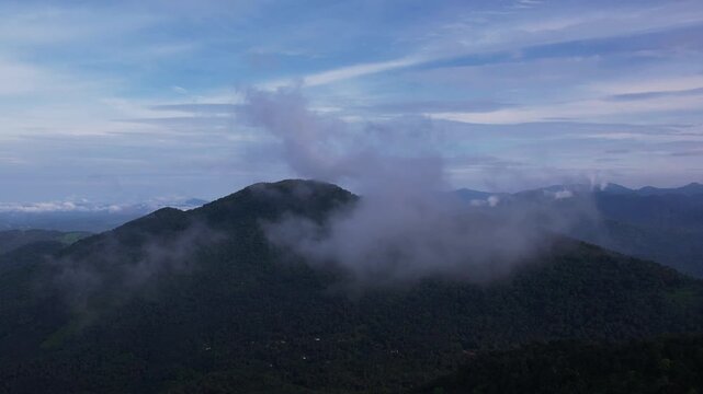 Aerial drone flying through thick clouds and mist over green mountain ridge and forested hills. Fog drifting across layered mountain range 