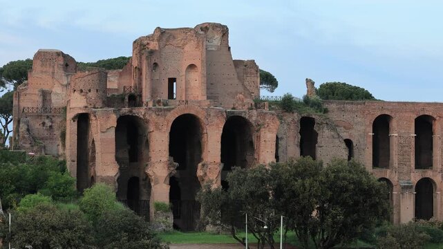 A wide shot showing the majestic brick arches and remains of the imperial palaces on the Palatine Hill. The ancient structures are surrounded by Mediterranean greenery an