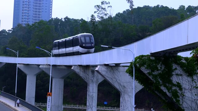 Modern urban elevated skyrail monorail train traveling through green city landscape under bright daylight 4K. futuristic urban public transportation system, featuring a sleek black and white monorail 