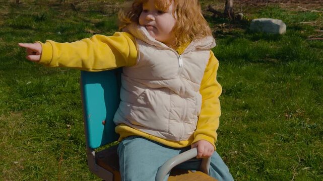 Redheaded girl playing on seesaw at playground. Happy female child having fun on teeter totter outdoors. Childhood activity, leisure time, recreation in park.