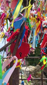 Red heart-shaped padlock symbolizing eternal love and romance, hanging tightly on a metal structure adorned with countless vibrant ribbons, representing wishes and devotion