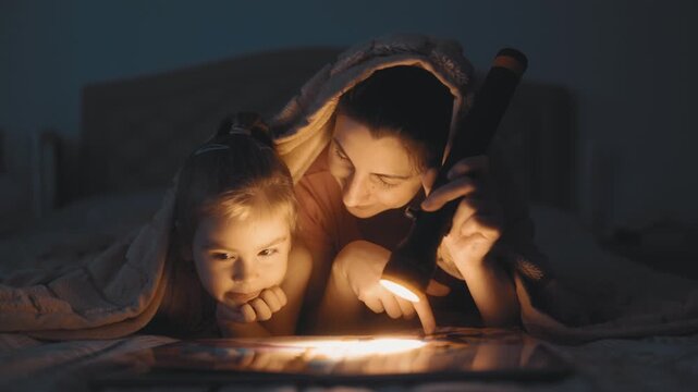 Mother and Young Daughter Reading Storybook With Flashlight lifestyle