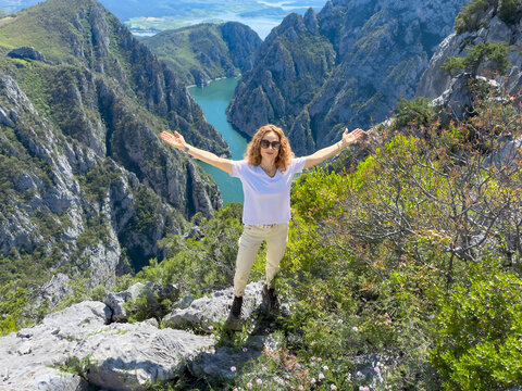 Hiker woman on the background of a mountain river. Girl traveler stands on the edge of rock