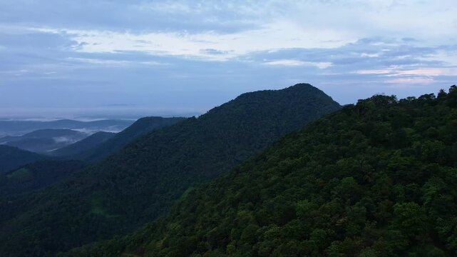 Aerial drone panoramic view of layered green mountains and deep valley with low clouds drifting above the landscap