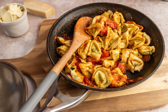 Tortellini in a skillet with sauce, tomatoes and basil on a stone surface 