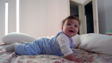 Fototapeta premium Baby lying on bed looking upward with curious expression, showing wonder and attentiveness in peaceful home environment