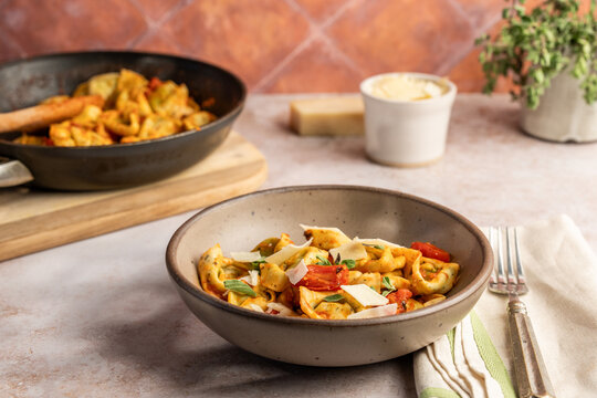 Tortellini in a pottery bowl with sauce, tomatoes and basil sprinkled with cheese on a stone surface 