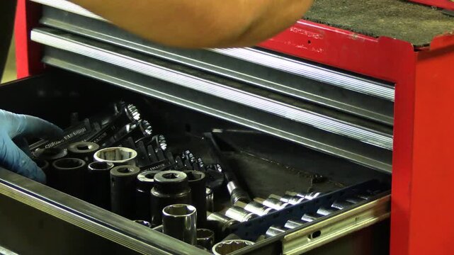 Hand holding extension bar while searching through a tool chest drawer for the correct socket. Disorganized tool storage, mechanic workflow, automotive repair preparation, garage environment, troubles