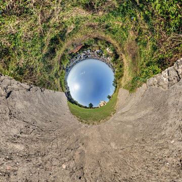 creative tiny planet photo of a rural landscape with dirt road, green fields, and cloudy sky forming a circular world.