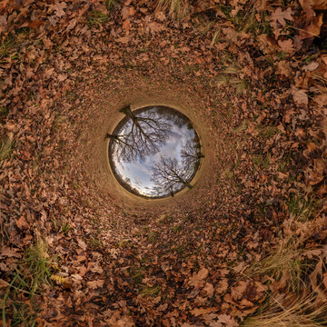creative tiny planet photo of a rural landscape with dirt road, green fields, and cloudy sky forming a circular world.