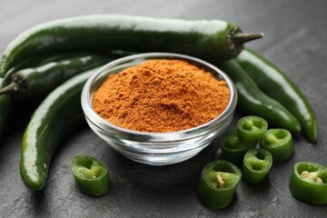 Fototapeta premium Powdered and raw chili peppers on black textured table, closeup