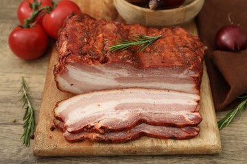 Fototapeta premium Pieces of smoked bacon, tomatoes and rosemary on wooden table, closeup