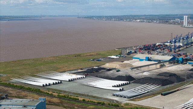 Aerial view of wind turbine blades stored at the industrial port area with the Humber Bridge in the distance at Salt End, England, United Kingdom.