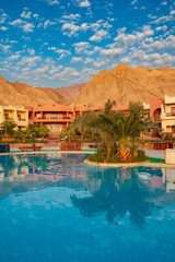 Obraz premium Vertical view of a luxury resort swimming pool with palm trees and Sinai mountains at sunset in Dahab, Egypt. 