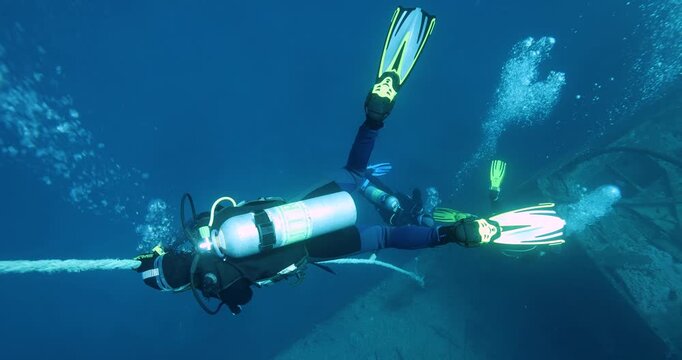 A group of divers diving towards a sunken ship SS Thistlegorm in the Red Sea. Divers descend together into a cloud of bubbles  around a guide rope. Summer vacation shot