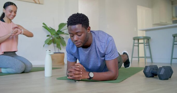 Fitness partners holding forearm plank on green mat at home while woman checking watch, timing set
