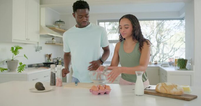 Couple in bright kitchen exchanging words, cracking eggs into glass bowl and seasoning breakfast