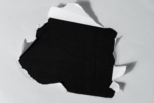 A rough tear hole in the center of a white sheet of paper against a contrasting, solid black background.