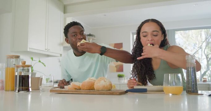 African American couple preparing breakfast on kitchen counter, man offering roll to share