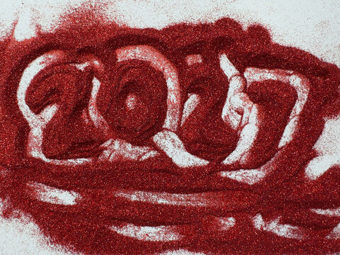 Red glittery sand forms the year 2027 on a white background. Shimmering texture catches light with vibrant intensity. Artistic abstract design for New Year celebrations or retro-themed projects