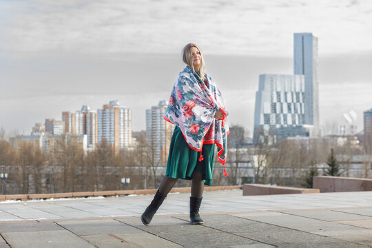 A young woman in a military dress and cap holds a beautiful fluttering scarf in a city square on May 9.
