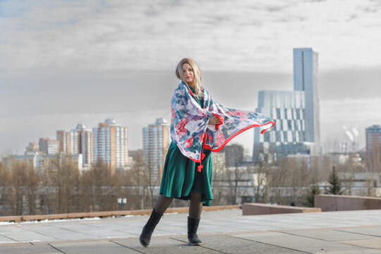 A young woman in a military dress and cap holds a beautiful fluttering scarf in a city square on May 9.