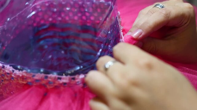 Horizontal 4K video close up. Female hands tying magenta tulle to elastic band. Woman making children's pink carnival tutu skirt. Concept of dance, craft, diy art work, ballet, diverse beauty, fashion