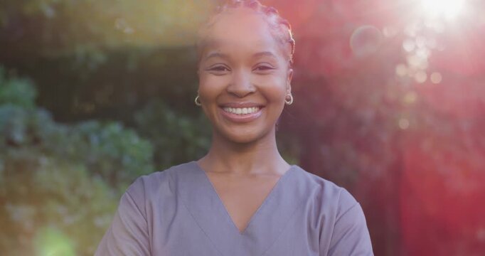 African woman reacting to sunlight shifting to broad smile as lens flare veiling garden in scrubs