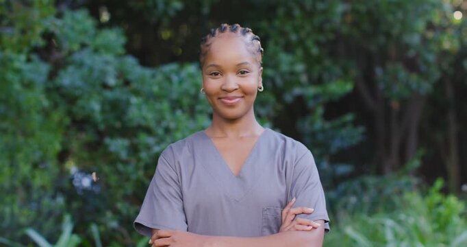 Woman in grey scrubs posing arms crossed in garden while camera panning and sunlight warming braids