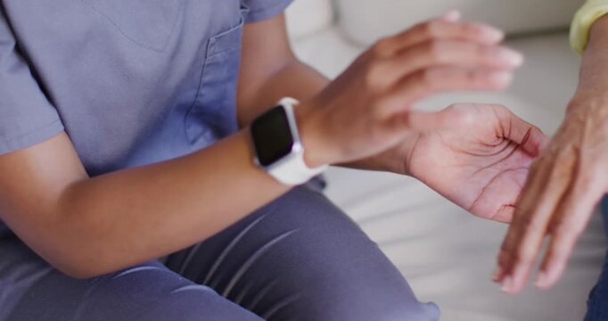 African American caregiver in scrubs holding senior's hand after reaching out, comforting on sofa