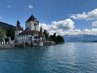 Fototapeta premium Panorama of Schloss Oberhofen am Thunersee - castle on the shore of Lake Thun with calm water and alpine scenery in Switzerland.