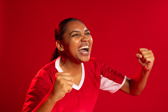 African woman cheering, clenching fists, wearing red jersey and stud earrings in studio