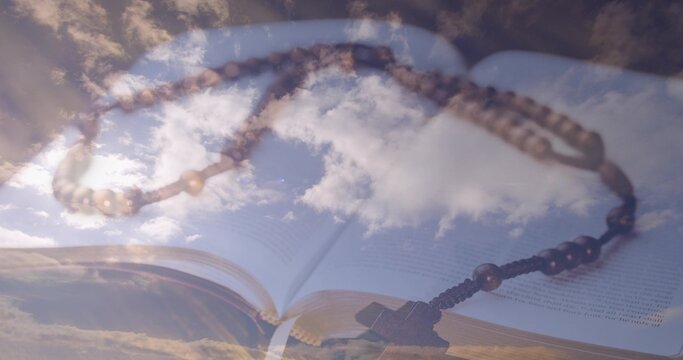 Lying rosary beads curving across open book pages in studio, cross pendant and page edges